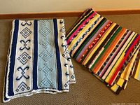 Both blue-white and multicolored afghans folded and laid next to each other on a carpeted floor.