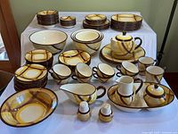 Large set of Vernonware Kilns dishes displayed on a table with various plates, bowls, cups, and serving pieces featuring a vintage brown and yellow swirl pattern.