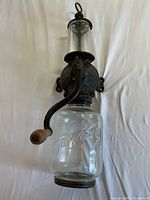 Full view of vintage coffee grinder with glass jar, cast iron mechanism labeled 'Crystal Arcade', featuring a wooden handle knob and clear glass hopper top.