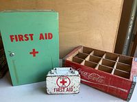 The green metal first aid box, the small white metal first aid box, and the red wooden Coca Cola crate