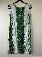 Full view of green and white batik sleeveless shift dress hanging on black plastic hanger