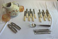 Wide view of the ceramic pitcher, amber glass bowls, flatware, nutcrackers, serving fork, and peelers on white tablecloth