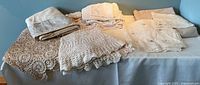 Five vintage linen and crocheted table linens laid out on table: mix of tablecloths, napkins and doilies in cream and beige tones.