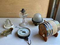 Nine vintage items including a hanging scale, glass insulator, oil lamp, dome light, small barrel, and brass figurine