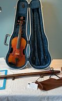Hard shell case open showing violin, bow and wood flute on table