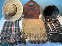 Full view of lot showing the straw cowboy hat, vintage tooled leather horse purse, three large fringed shawls laid flat, and a dark woven basket.