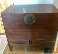 Front view of the wooden chest showing the brass latch and two lower drawers with round pulls.