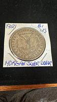 Photo of the back of the 1921 Morgan Silver Dollar showing the eagle design and handwritten notes on the holder