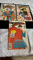 Three pre-owned Superman comic books displayed on a table, showing front covers of the December 1987, January 1988, and April 1988 issues
