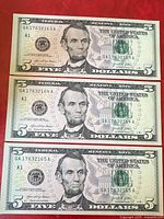 Front view of three consecutive 2021 U.S. $5 bills showing Abraham Lincoln portrait, serial numbers QA17632163A, QA17632164A, QA17632165A, and 'A1' series mark.