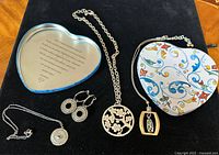 Photo showing three Brighton necklaces, one pair of silver-tone circular patterned earrings, and a decorative heart-shaped colorful floral tin with printed message inside lid.