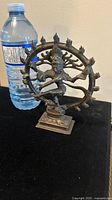 Full front view of cast brass Shiva Nataraja statue next to a water bottle for size reference.