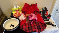 Overview of lot including dog feeding bowl, red corduroy coat, pink floral harness and leash, and floral harness.