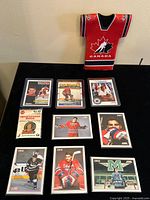 Overview photo showing nine Eric Lindros hockey cards spread on a black surface and a red jersey shaped Team Canada pin in unopened package.