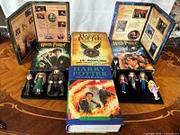 Photo showing the 3 hard cover books (Harry Potter and the Cursed Child, Half-Blood Prince, Prisoner of Azkaban), 2 DVDs, and 8 mini Harry Potter figures arranged on table