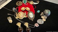 Overview of vintage silver and gold-plated costume jewelry spread out on black cloth with a red pouch centerpiece.