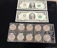 Top view showing a $1 and $2 bill and twelve quarters in plastic holders, arranged in two rows of six coins each