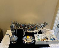 Front view of lot including large metal centerpiece, boxed shot glasses, brass Surahi, and mosaic bowl