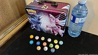 Photo showing the metal Pokemon carry case with artwork of Dialga and Palkia alongside 14 colorful Pokemon marbles arranged in front.