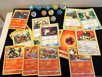 Photo showing a collection of 30 Pokémon cards including Flareon, Charmeleon, Houndour, Salandit, along with Trainer cards such as Switch and Pokémon Fan Club, displayed on a flat surface with 10 Pokémon-themed marbles arranged above them.