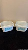 Two vintage Pyrex Amish Butterprint 501B refrigerator dishes with lids on black cloth against wall, showing front pattern.