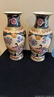 Pair of vintage hand painted Satsuma vases displayed upright on a black cloth, showing the detailed artwork including traditional figures and floral patterns