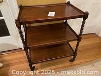 Full view of antique oak barleytwist tea trolley showing three shelves and wheels on the legs.