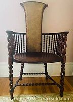 Front view of antique wooden armchair showing tall upholstered back with floral fabric, turned spindle arms, and carved wooden seat.