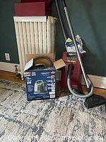 Photo showing the Miele vacuum cleaner upright and the Little Green carpet cleaner box beside it, on a carpeted floor near a radiator.