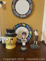 Shows two colorful ceramic dishes, Mr. Peanut cookie jar, and two sports figurines on a shelf against a yellow wall.