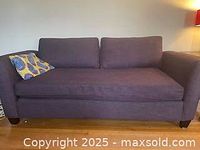 Full front view of the dark gray fabric daybed with two back cushions and one seat cushion, placed against a light wall with a wooden floor beneath.