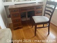 Front view of wooden kneehole desk with multiple drawers and upholstered chair