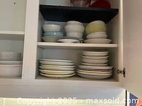 Three shelves filled with mostly white ceramic plates, bowls, and platters. Some bowls have pastel-green and blue tones.