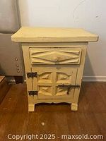 Front view of yellow bedside chest showing drawer with knob and cabinet door with two metal hinges and latch, carved paneling detail on the door.