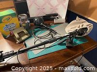 Desktop view showing Blue Snowball USB microphone on boom arm with cable, staple gun, cutting board, Crayola crayons, and bulletin board corner in background.