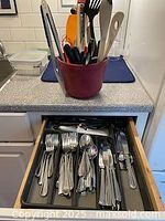 Photo showing kitchen utensils stored in a red container on the countertop, including tongs, spoons, and spatulas
