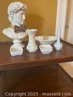 Wide view of all white porcelain items on wooden shelf including bust, bowls, and vases