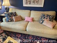 Whittington cream-colored sofa with down cushions, showing the left side with patterned and solid color throw pillows, situated in a living room area with a patterned rug and a lamp on the side.
