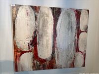 Front view of large abstract painting with white and gray oval shapes on red and brown background.