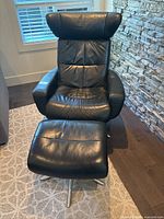 Front view of black leather reclining armchair with ottoman against stone wall and window