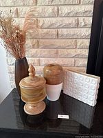 Front view of all decorative items including wooden jar, ceramic vase, black vase with dried flowers, and white ceramic wall tile