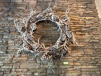 Front view of large frosted pinecone Christmas wreath against stone wall.