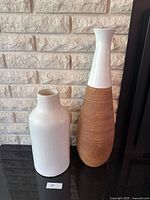 Two large vases shown side by side against a brick wall background on a black surface, showcasing their shape and color.
