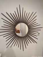 Front view of a decorative sunburst wall mirror hung on a wall, showing the full mirror and its metal frame with pointed rays radiating outward.