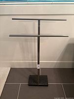 Front view of the modern stainless steel towel rack with two towel bars and black rectangular base against a white wall.