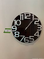 Photo of a modern round wall clock with black face and large white numerals from 1 to 12, silver clock hands indicating the time 12:10.