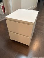 View of one white modern nightstand with two drawers on dark wood floor, minor wear visible.