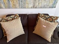Four decorative pillows on a dark couch: 2 beige textured pillows and 2 hexagon-patterned pillows with oranges and browns
