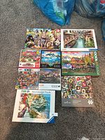 Photo showing eight boxed puzzles laid out on floor, including animals, landscapes, and collage themes.