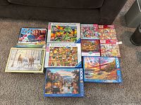 Overview of 10 puzzle boxes arranged on carpet beneath couch, showing variety of images and piece counts